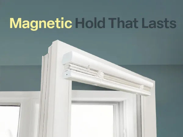 Close-up of a white magnetic cordless mini blind mounted to the top of a white metal door frame, shown in a folded-up position against a teal-colored wall.