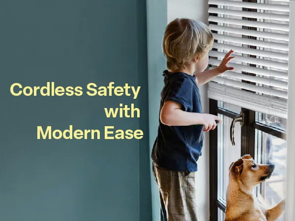 A young child and a dog looking out of a glass door covered with white cordless horizontal blinds. The text 'Cordless Safety with Modern Ease' is displayed on a teal wall to the left.