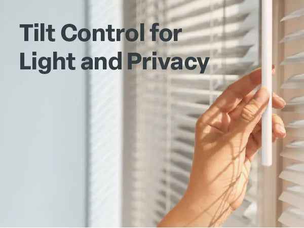 Close-up of a person's hand turning a white tilt wand on a set of white horizontal mini blinds. Sunlight filters through the slats, creating shadows on the hand. Text at the top left reads 'Tilt Control for Light and Privacy'.